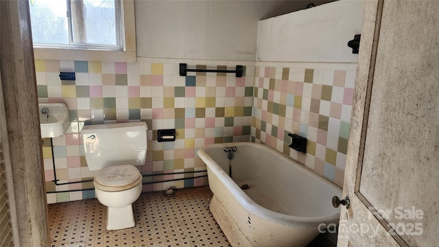 full bath featuring toilet, a bathing tub, tile walls, and wainscoting