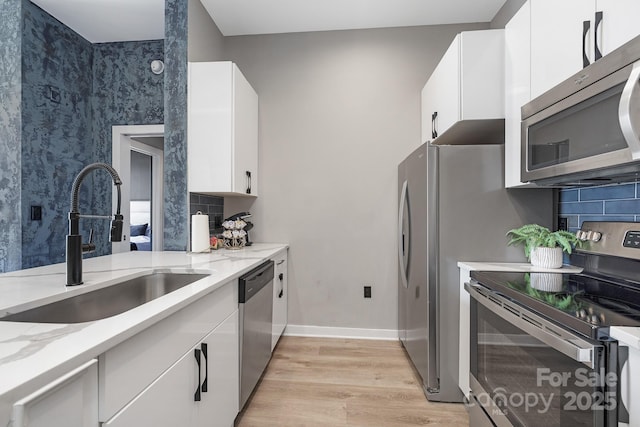 kitchen with light wood-type flooring, a sink, stainless steel appliances, decorative backsplash, and light stone countertops