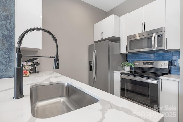 kitchen with tasteful backsplash, light stone countertops, appliances with stainless steel finishes, white cabinets, and a sink