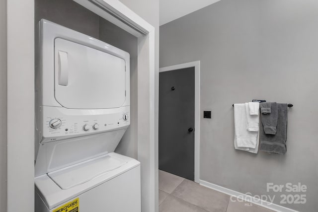 washroom featuring baseboards, stacked washer and clothes dryer, light tile patterned flooring, and laundry area