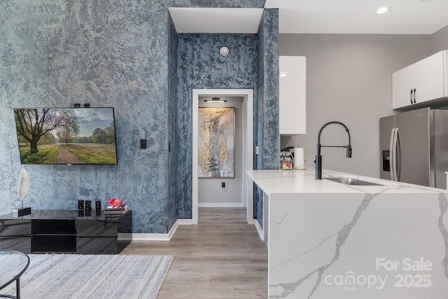 kitchen featuring light stone countertops, baseboards, stainless steel fridge with ice dispenser, white cabinets, and light wood-style floors