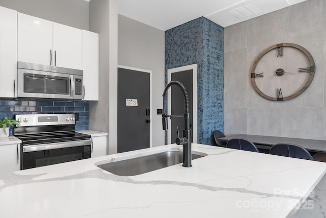 kitchen with a sink, white cabinetry, appliances with stainless steel finishes, decorative backsplash, and light stone countertops