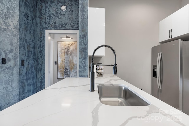 details with white cabinetry, light stone countertops, stainless steel refrigerator with ice dispenser, and a sink