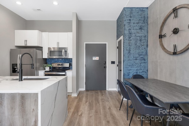 kitchen with light stone counters, light wood finished floors, stainless steel appliances, white cabinetry, and tasteful backsplash