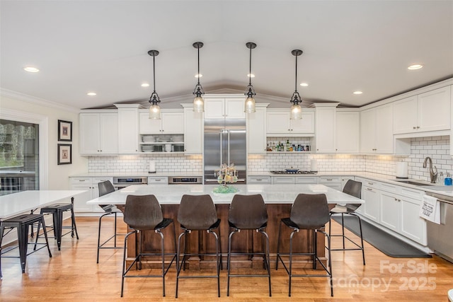 kitchen with stainless steel appliances, a kitchen island, a sink, light wood-style floors, and white cabinets