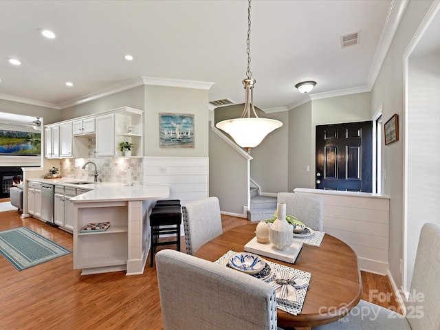 dining area with light wood-type flooring, visible vents, crown molding, and stairway