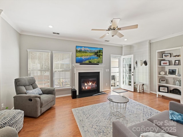 living room featuring ornamental molding, a glass covered fireplace, wood finished floors, and visible vents