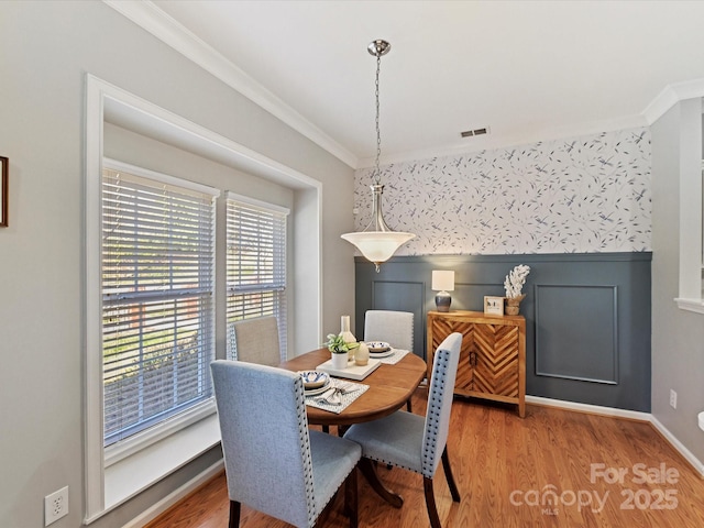 dining room with a wainscoted wall, visible vents, crown molding, and light wood finished floors