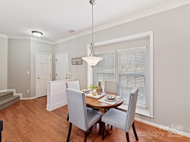 dining room with light wood finished floors, baseboards, visible vents, stairway, and crown molding