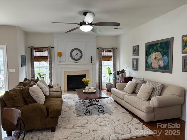 living area with a ceiling fan, wood finished floors, a fireplace, and visible vents