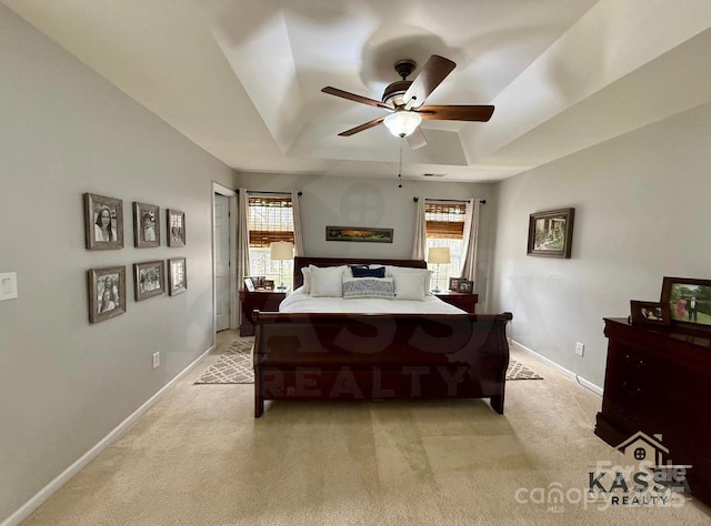 bedroom featuring light carpet, ceiling fan, baseboards, and a tray ceiling