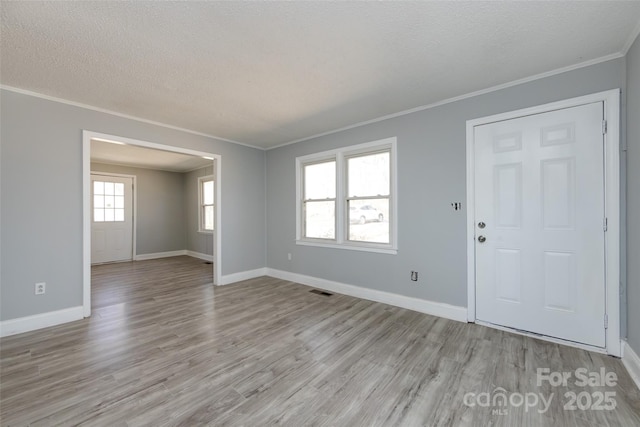 empty room with ornamental molding, light wood finished floors, a textured ceiling, and baseboards