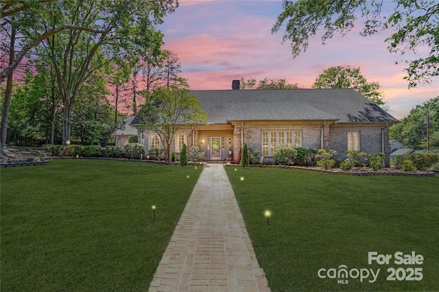 view of front of property featuring a chimney, a lawn, and brick siding