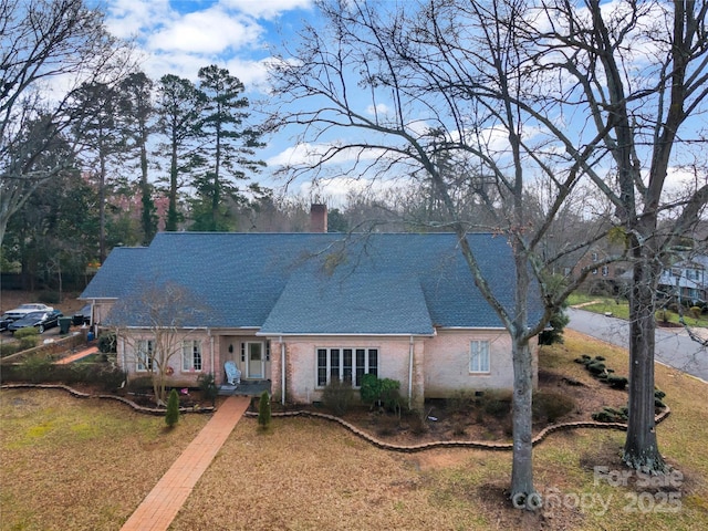 view of front of property featuring a shingled roof, brick siding, and a chimney