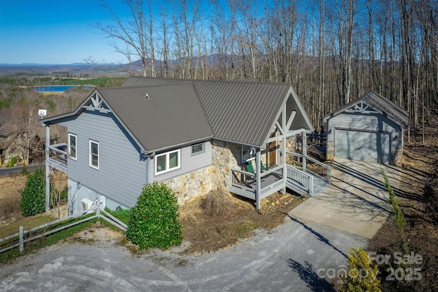 rear view of property with metal roof, driveway, stone siding, and an outbuilding