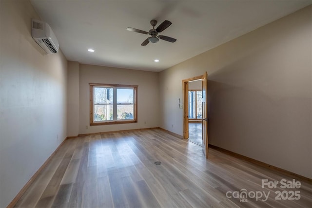 unfurnished room with light wood-type flooring, an AC wall unit, a healthy amount of sunlight, and baseboards