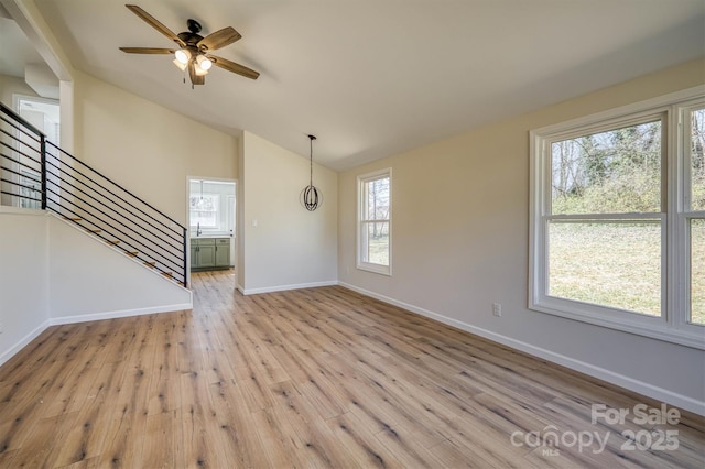 unfurnished living room featuring lofted ceiling, stairway, light wood finished floors, baseboards, and ceiling fan