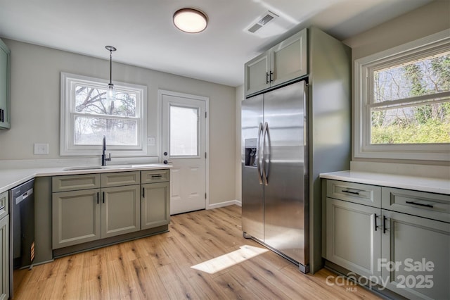 kitchen with light wood-type flooring, visible vents, a sink, stainless steel appliances, and light countertops