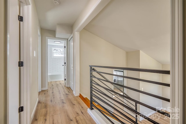 hall featuring an upstairs landing, light wood-style flooring, lofted ceiling, and baseboards