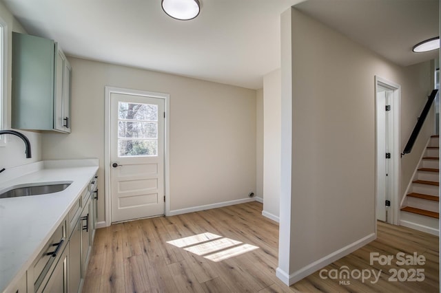 kitchen featuring a sink, baseboards, light stone countertops, and light wood finished floors