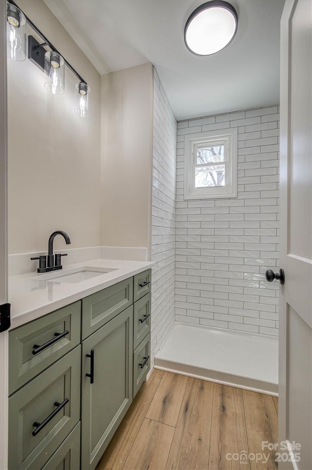 bathroom with tiled shower, vanity, and wood finished floors