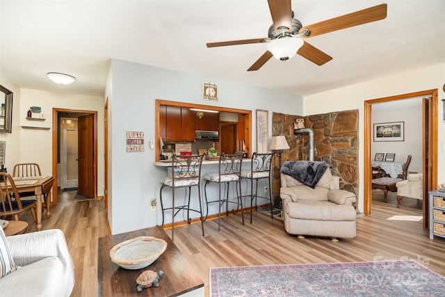 living area featuring ceiling fan, wood finished floors, and a wood stove