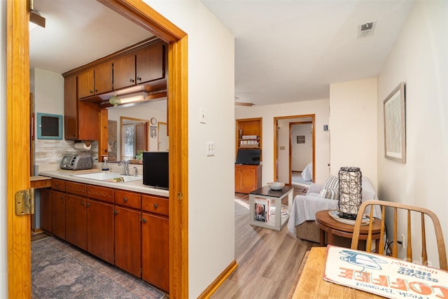 kitchen featuring a toaster, light countertops, decorative backsplash, a sink, and wood finished floors