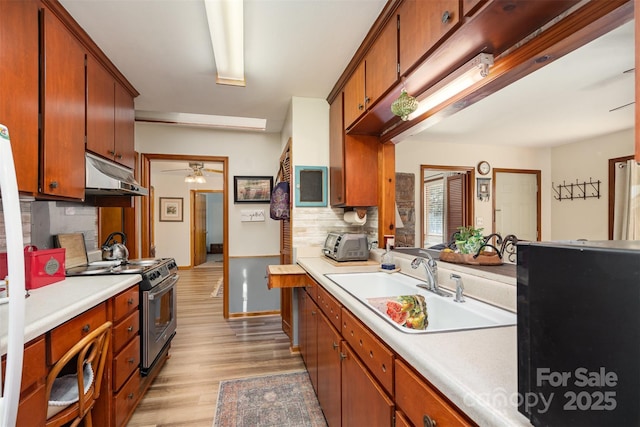 kitchen featuring light countertops, a sink, light wood-type flooring, under cabinet range hood, and stainless steel electric range