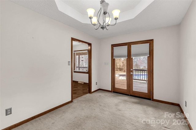 unfurnished room with carpet, french doors, a tray ceiling, and an inviting chandelier