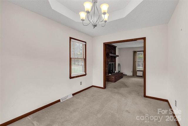 empty room featuring a tray ceiling, visible vents, a notable chandelier, and a fireplace