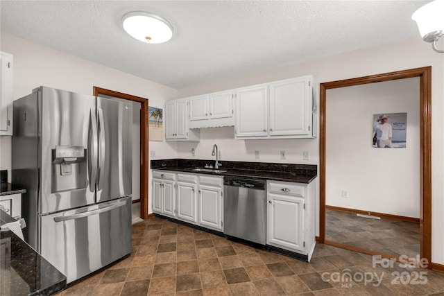 kitchen featuring stainless steel appliances, a sink, white cabinetry, baseboards, and dark stone countertops