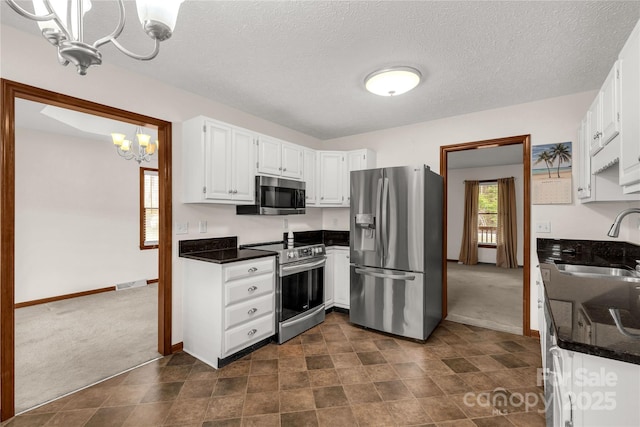 kitchen with a sink, stainless steel appliances, dark colored carpet, and an inviting chandelier