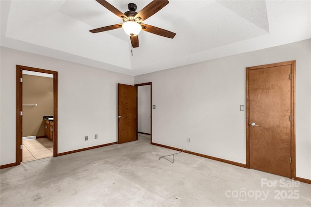 spare room with light carpet, a raised ceiling, a ceiling fan, and baseboards