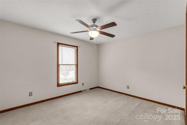 unfurnished room featuring light colored carpet, visible vents, ceiling fan, a textured ceiling, and baseboards