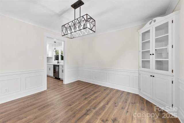 unfurnished dining area with dark wood-style floors, crown molding, a sink, and a notable chandelier