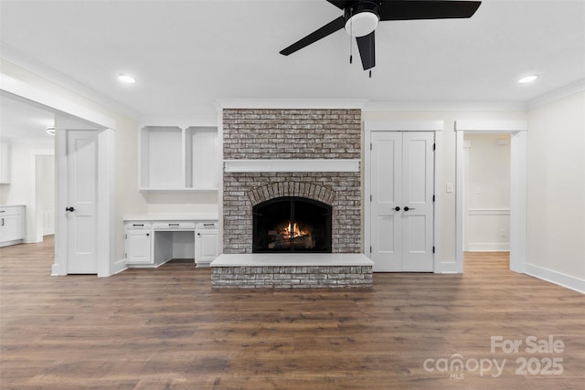 unfurnished living room with wood finished floors, baseboards, ornamental molding, a brick fireplace, and built in study area