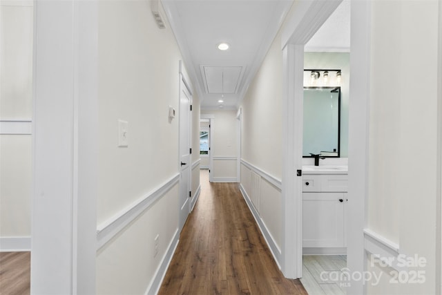 hall featuring attic access, wainscoting, a decorative wall, and wood finished floors