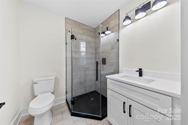 bathroom with a stall shower, baseboards, vanity, and toilet