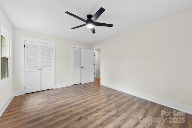 unfurnished bedroom featuring ceiling fan, wood finished floors, two closets, and baseboards