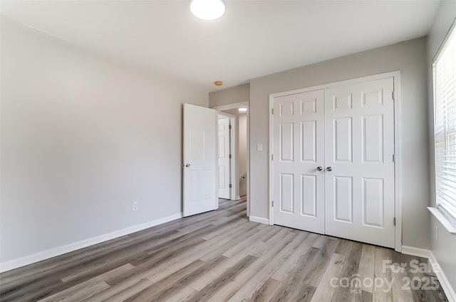 unfurnished bedroom featuring light wood-type flooring, a closet, and baseboards