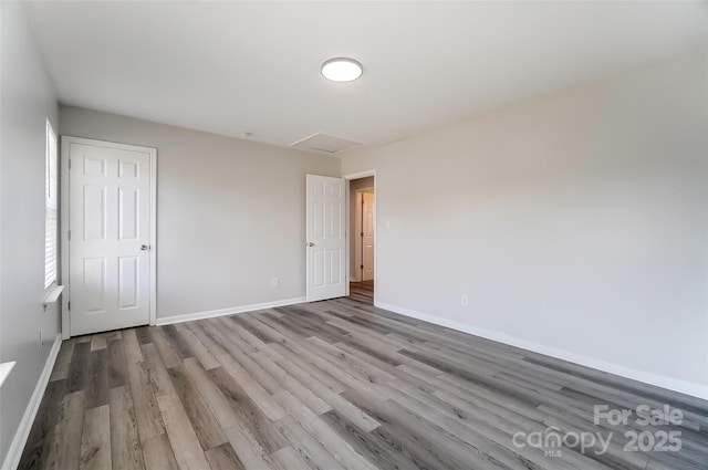 unfurnished bedroom with attic access, baseboards, and wood finished floors