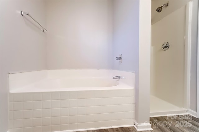 bathroom with a garden tub, wood finished floors, walk in shower, and baseboards