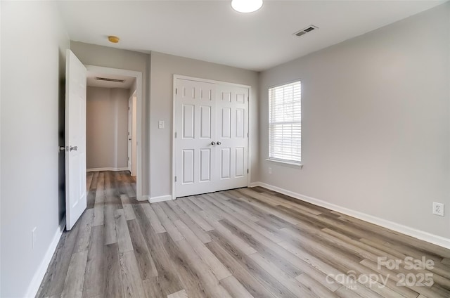 unfurnished bedroom with a closet, light wood-type flooring, visible vents, and baseboards