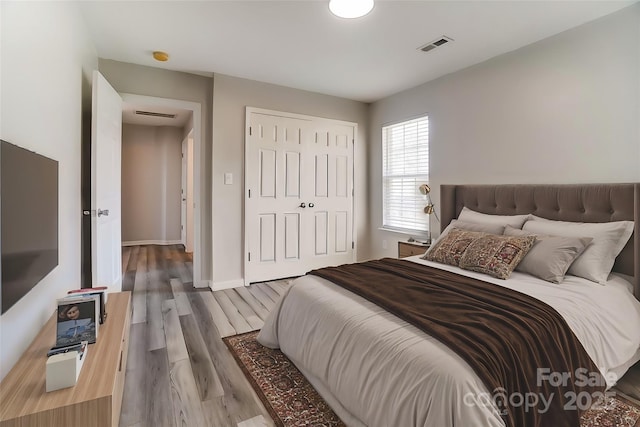 bedroom featuring a closet, wood finished floors, visible vents, and baseboards