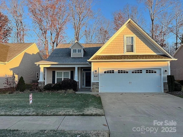 craftsman house featuring an attached garage, stone siding, driveway, and a front yard