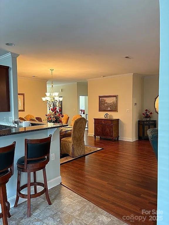 interior space with a breakfast bar, a notable chandelier, dark countertops, open floor plan, and wood finished floors