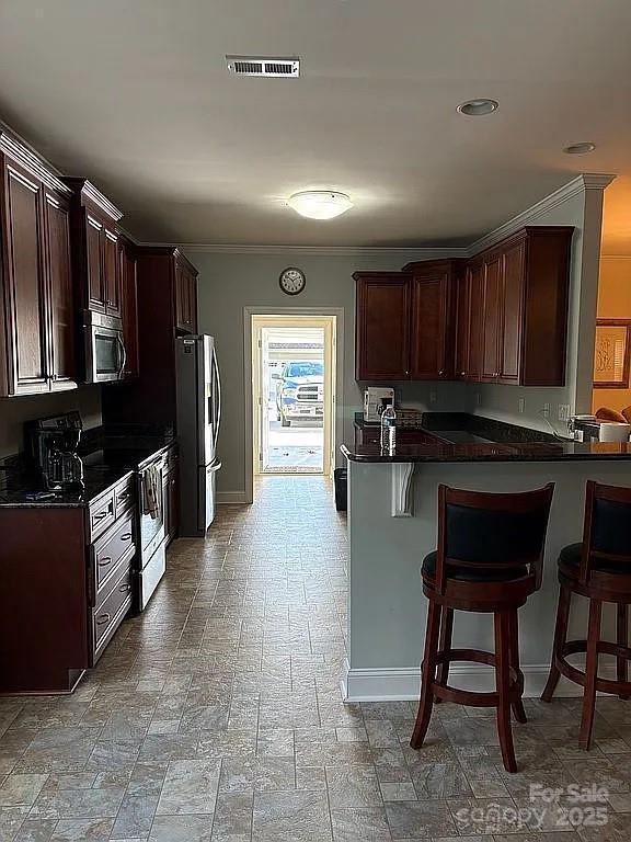 kitchen featuring appliances with stainless steel finishes, dark countertops, crown molding, and a breakfast bar area