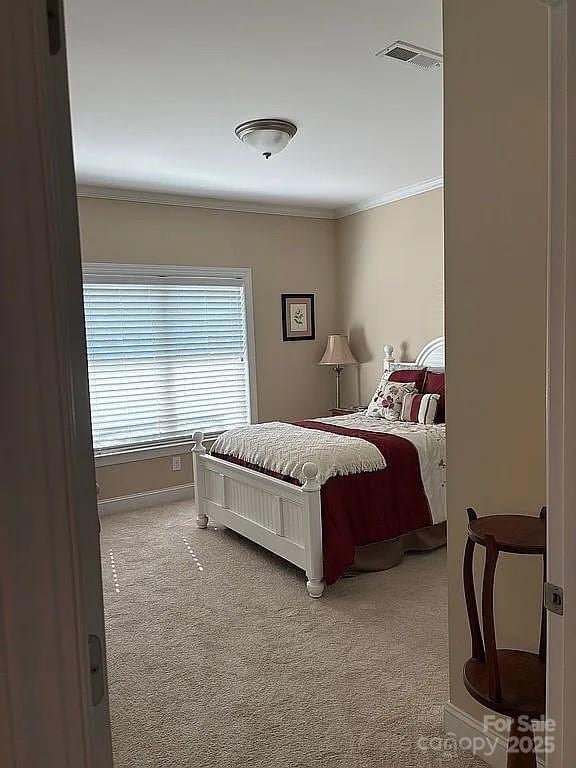 bedroom with light carpet, crown molding, visible vents, and baseboards