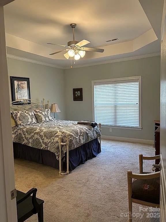 carpeted bedroom with crown molding, a raised ceiling, visible vents, ceiling fan, and baseboards