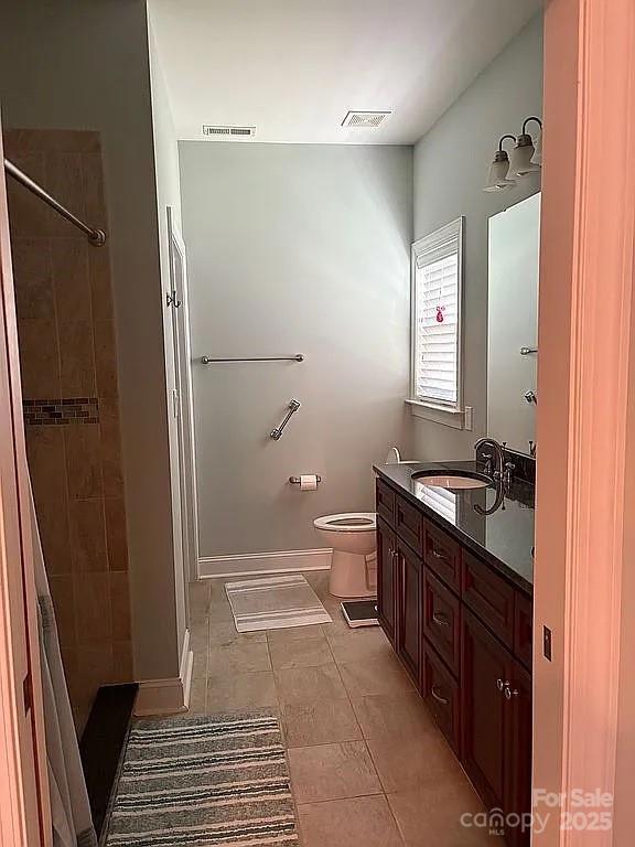 bathroom with toilet, visible vents, a tile shower, and vanity